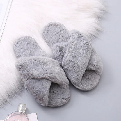 Gray fuzzy slippers on a light gray surface with a small bottle of perfume.