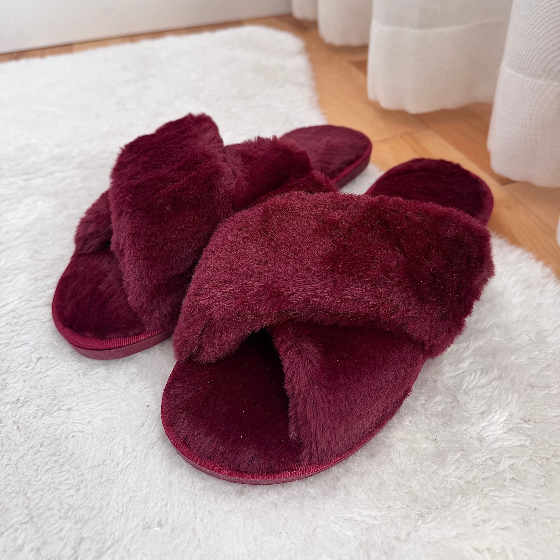 Pair of maroon fuzzy slippers on a white rug