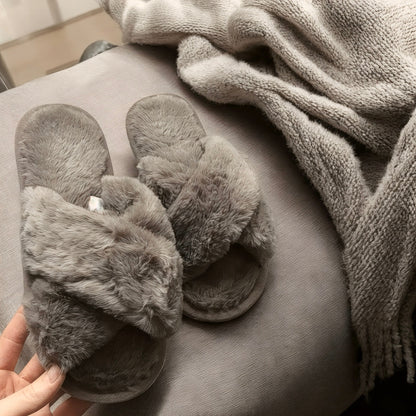 Gray fuzzy slippers on a cushion with a blanket in the background