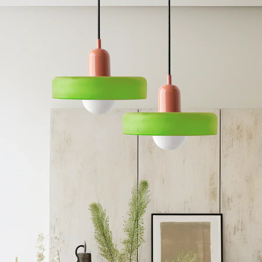 Two green pendant lights with pink bases hanging against a light-colored wall.