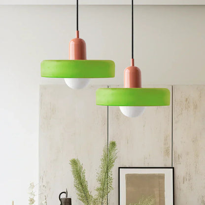 Two green pendant lights with pink bases hanging against a light-colored wall.