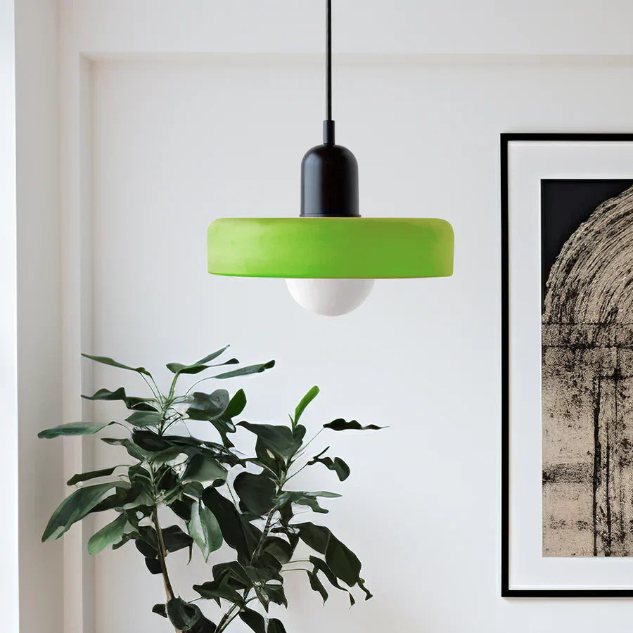 Green pendant light hanging in a room with a plant and framed artwork on the wall.