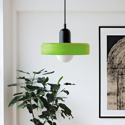 Green pendant light hanging in a room with a plant and framed artwork on the wall.