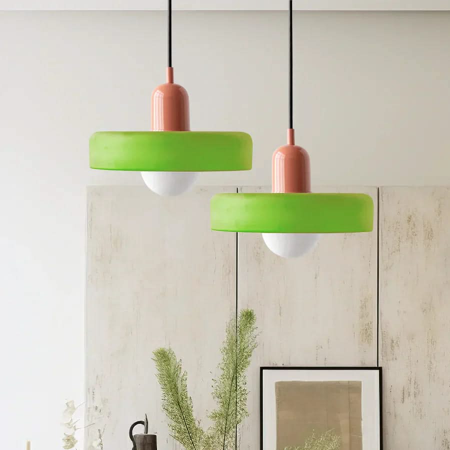 Two green pendant lights with pink bases hanging against a light-colored wall.