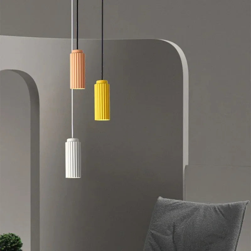 Three colorful pendant lights hanging against a gray wall with a gray cushion on a chair.