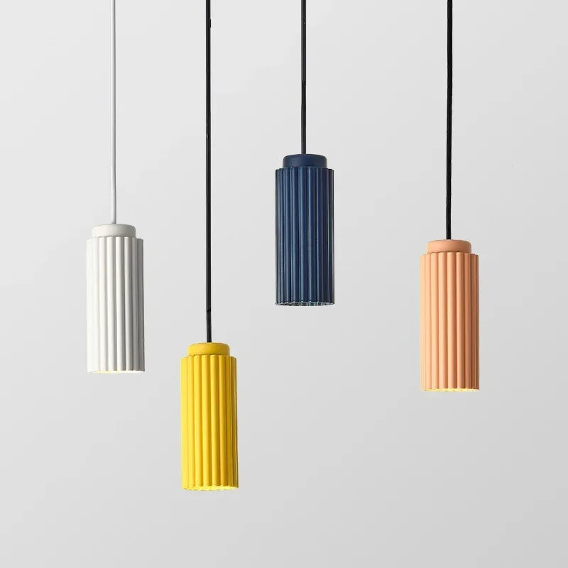 Five cylindrical pendant lights in different colors hanging against a light gray background