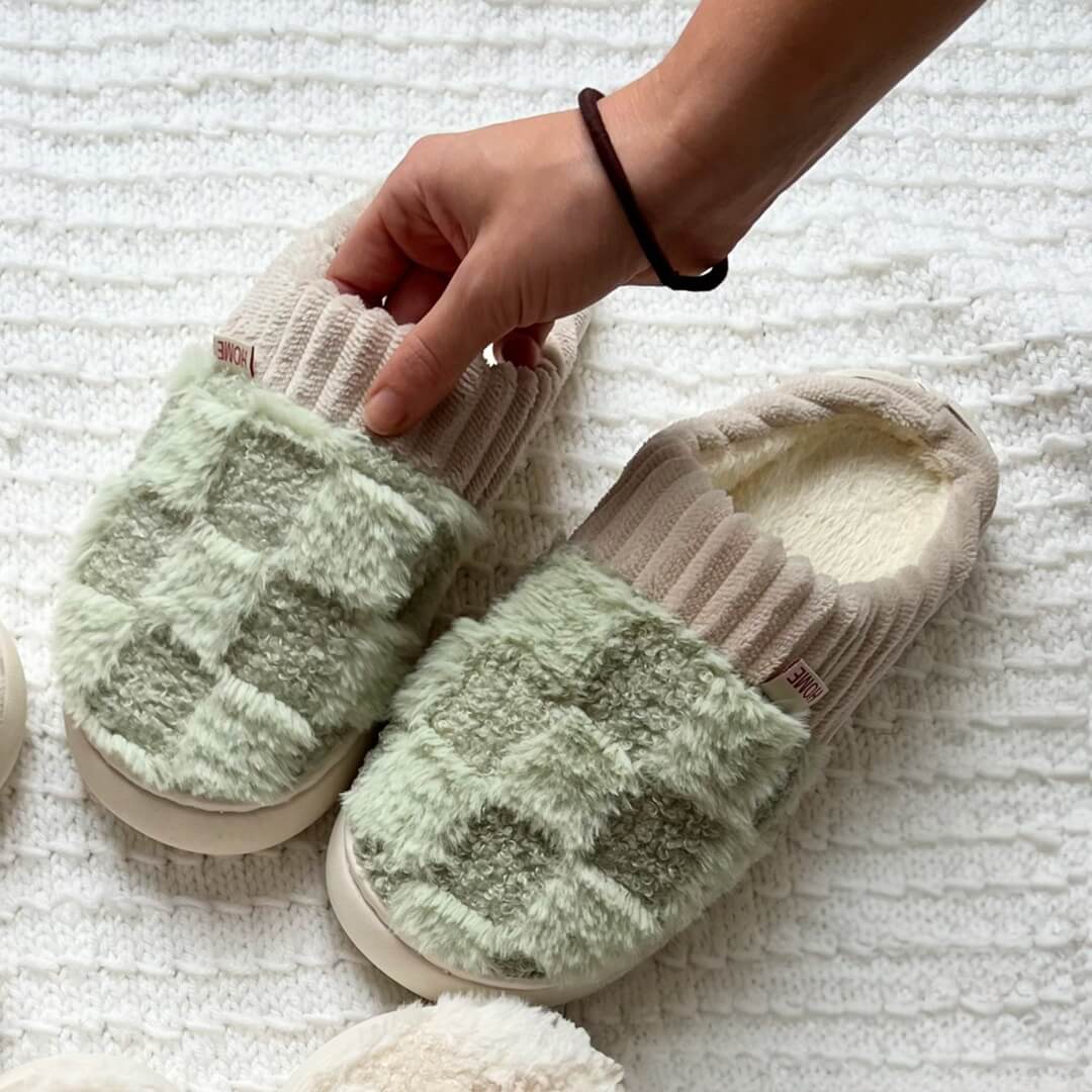 Pair of slippers with green fuzzy interior on a textured white surface