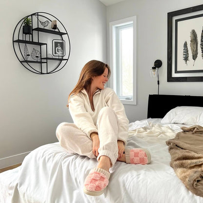 Woman sitting on a bed wearing pink fuzzy socks in a cozy bedroom.