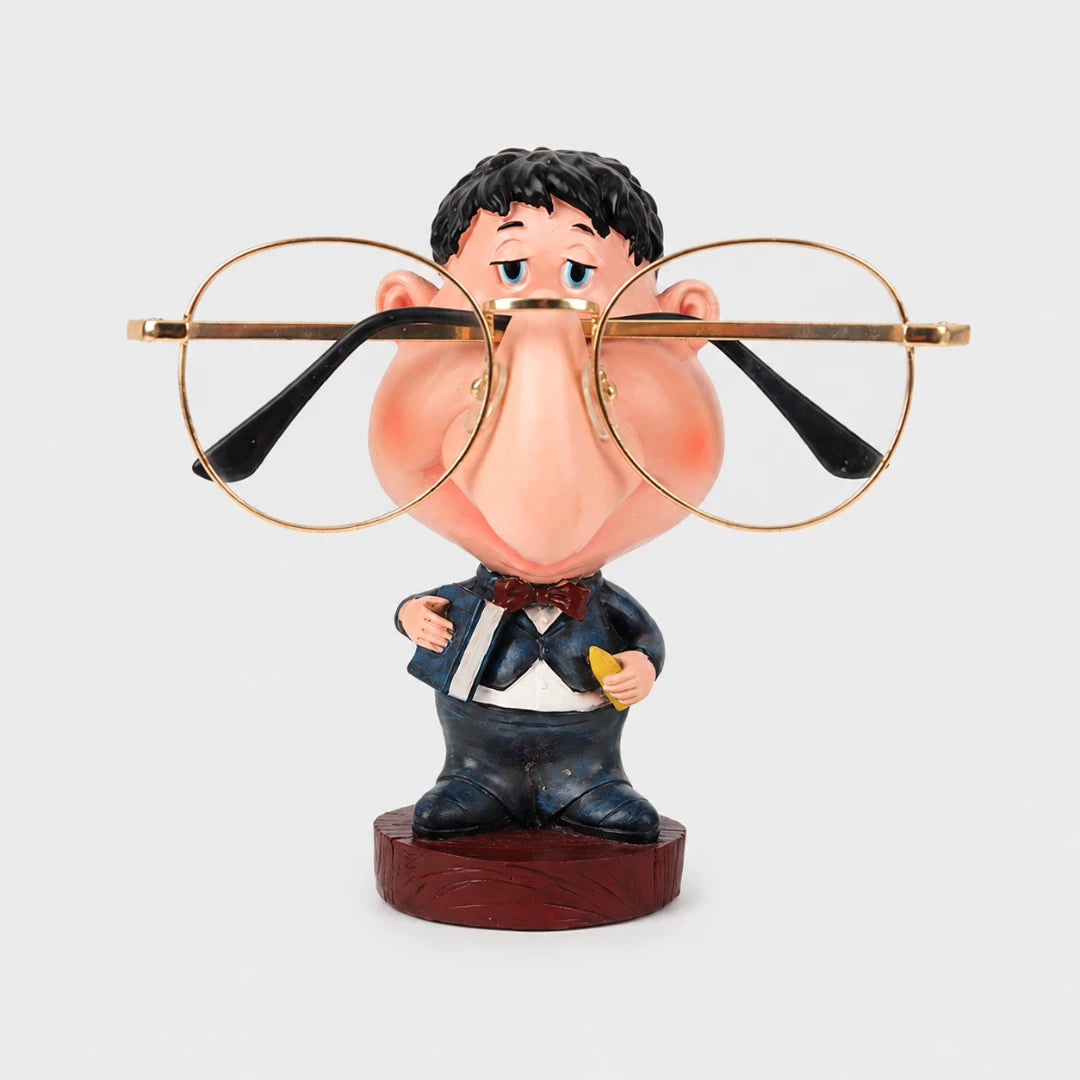 Josh & Tate - NoseNook™ Glasses Figurine Stand - A novelty figurine of a cartoon man with a large nose wearing oversized round gold-framed glasses, posed on a dark wood base against a light gray background.