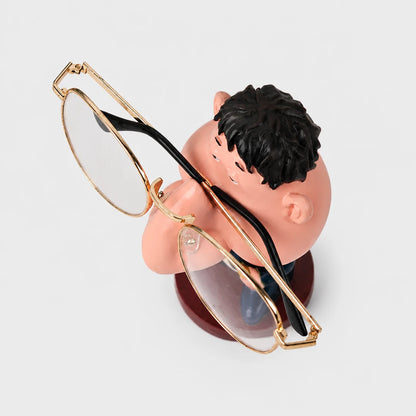 Josh & Tate - NoseNook™ Glasses Figurine Stand - A pair of round gold-framed eyeglasses with clear lenses and black temples, displayed on a small decorative stand shaped like a sleeping cartoon boy against a light gray background.