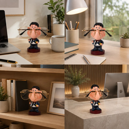 Josh & Tate - NoseNook™ Glasses Figurine Stand - A novelty desk accessory shown in a four-panel collage: a small cartoon figurine holding a pair of oversized round eyeglasses on a wooden desk, next to a laptop, mug, books, and other office items. The same product is also shown on a shelf and on a stone countertop in different home-office settings.