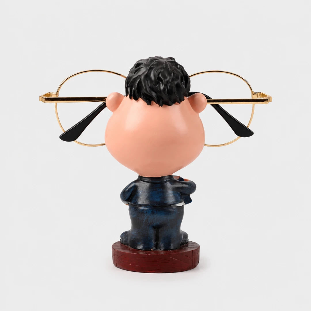 Josh & Tate - NoseNook™ Glasses Figurine Stand - A novelty bobblehead figurine of a man with a large peach-colored head, black hair, and a dark blue suit standing on a round wooden base, holding gold-framed eyeglasses behind his head.