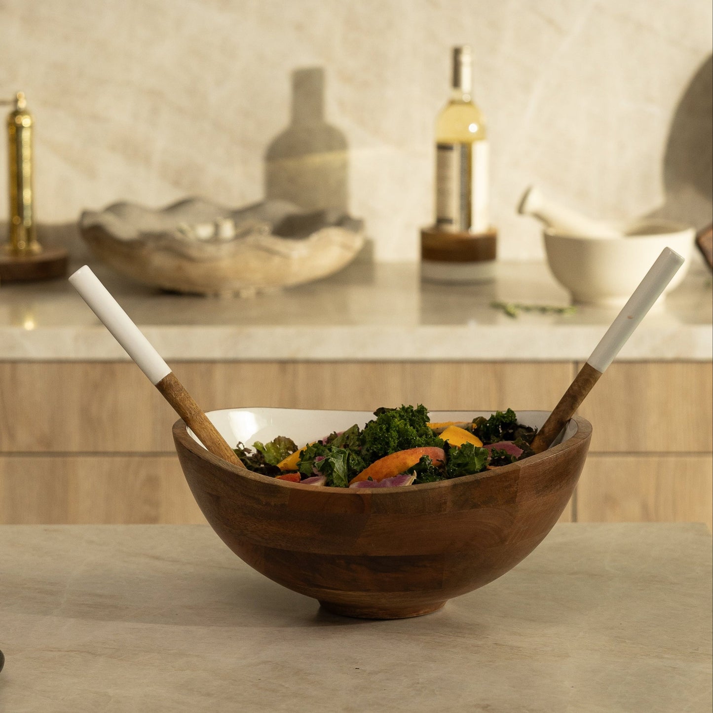 Wooden salad bowl with salad and utensils on a kitchen counter