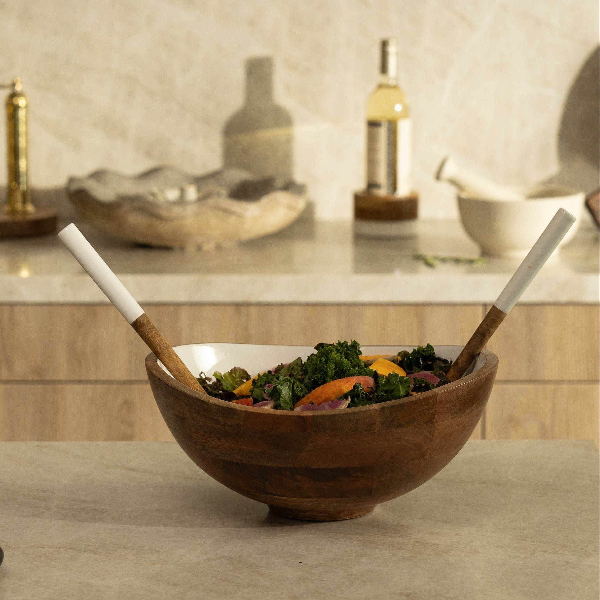 Wooden salad bowl with salad and utensils on a kitchen counter