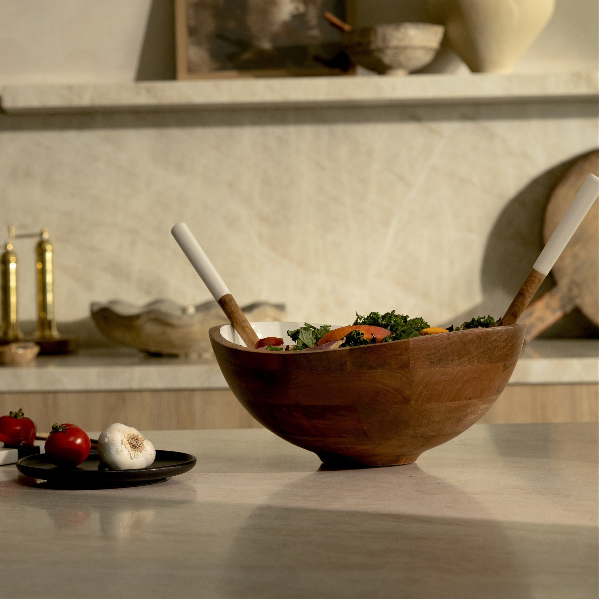 Wooden salad bowl with salad and utensils on a kitchen counter