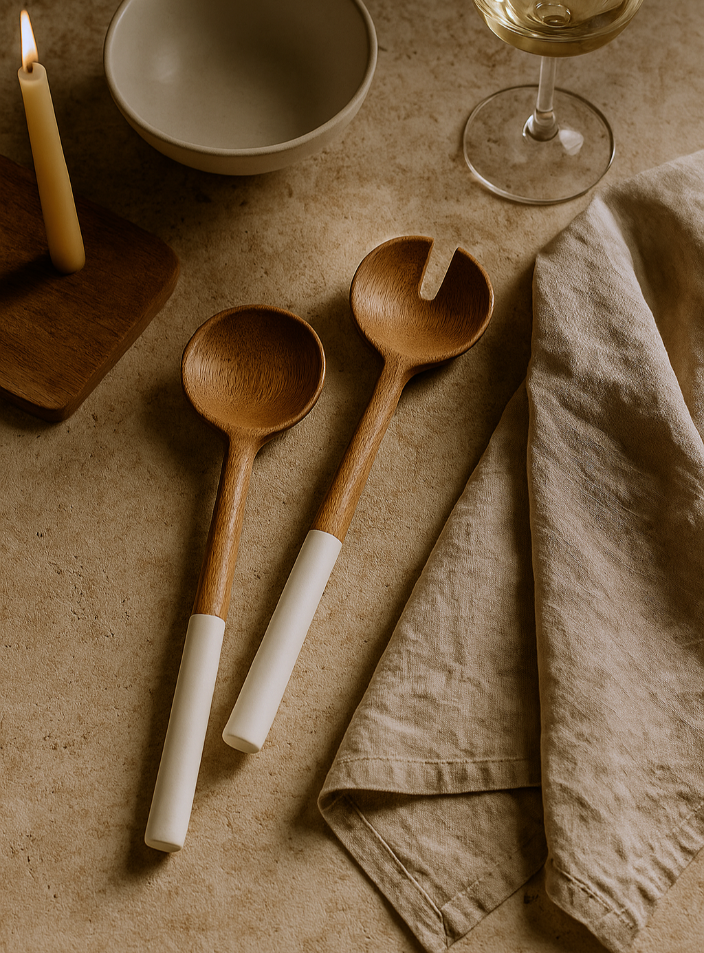 Wooden spoons with white handles on a textured surface with a candle and glass.