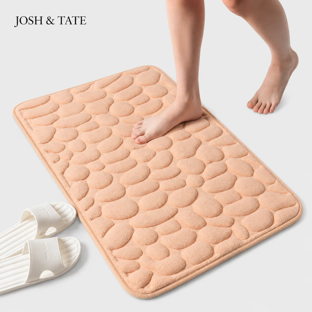 Josh & Tate - PebbleSoft™ Non-Slip Memory Foam Mat - Pink textured bath mat with a person stepping onto it, on a light gray background.