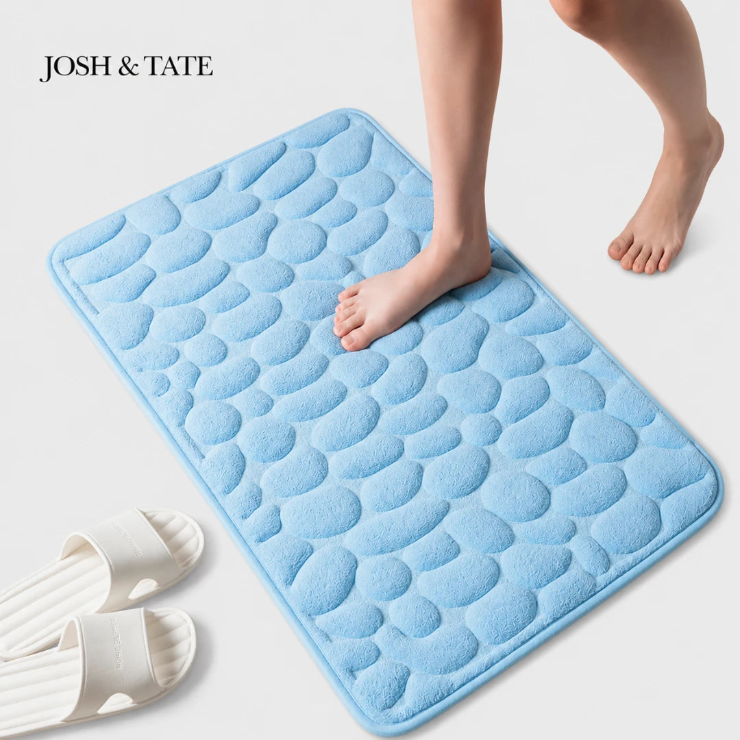 Josh & Tate -PebbleSoft™ Non-Slip Memory Foam Mat - Blue textured bath mat with feet stepping onto it, on a light gray background.
