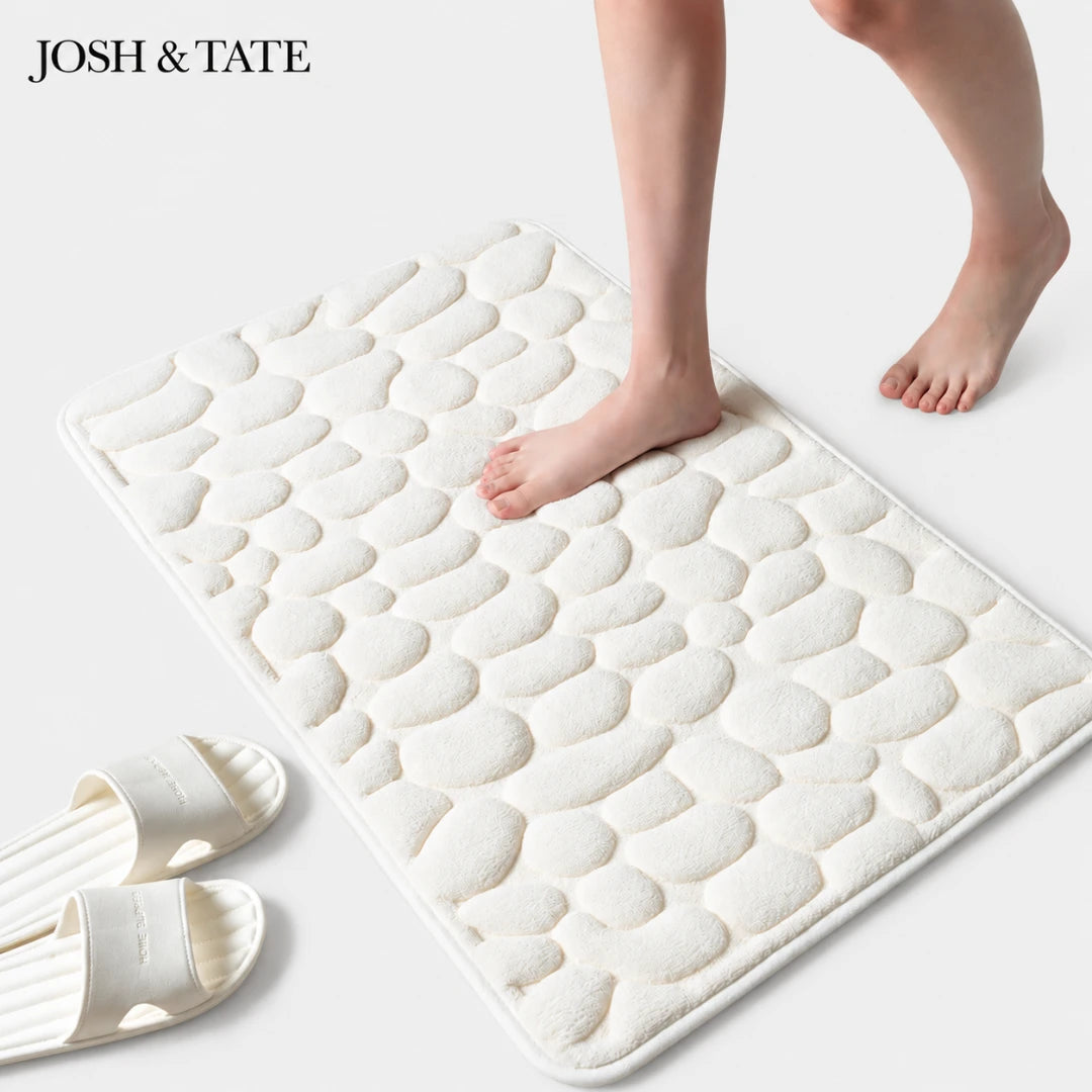 White textured bath mat with feet stepping onto it, featuring the brand 'Josh & Tate'.