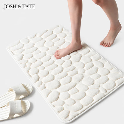 White textured bath mat with feet stepping onto it, featuring the brand 'Josh & Tate'.