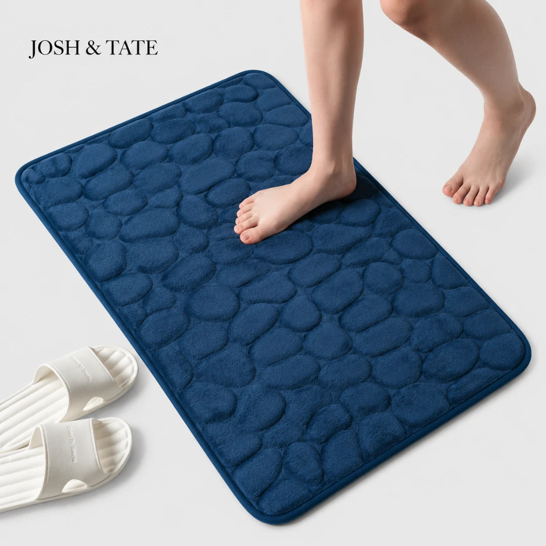 Josh & Tate - PebbleSoft™ Non-Slip Memory Foam Mat - Navy blue textured bath mat with a person stepping onto it, on a light gray background.