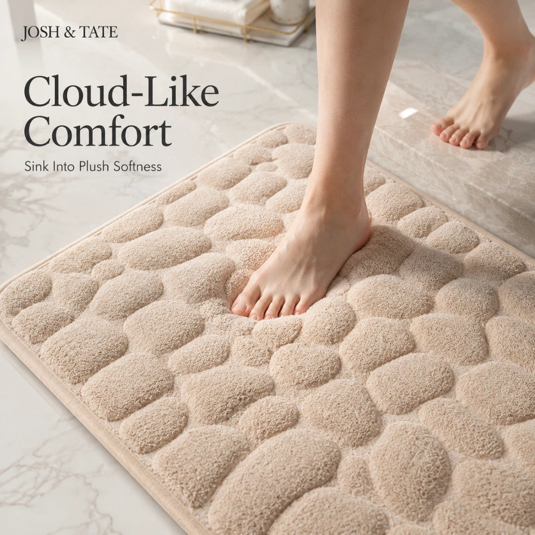 Josh & Tate - PebbleSoft™ Non-Slip Memory Foam Mat - Beige textured bath mat with feet stepping onto it, featuring 'Josh & Tate' branding.