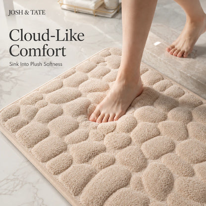 Josh & Tate - PebbleSoft™ Non-Slip Memory Foam Mat - Beige textured bath mat with feet stepping onto it, featuring 'Josh & Tate' branding.