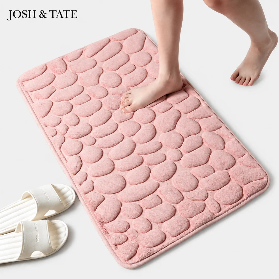 Josh & Tate - PebbleSoft™ Non-Slip Memory Foam Mat - Pink textured bath mat with feet stepping onto it, on a light gray background.