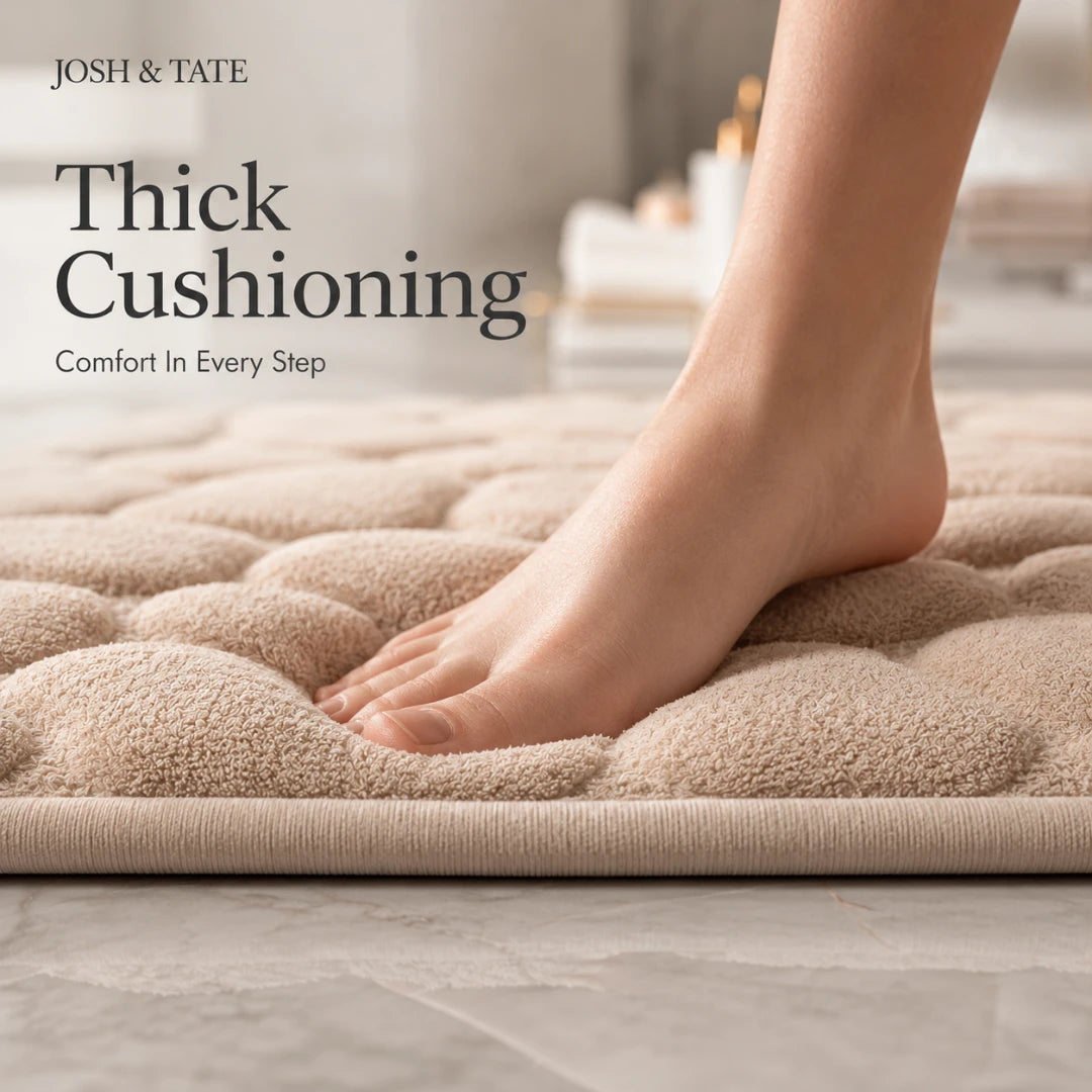 Josh & Tate - PebbleSoft™ Non-Slip Memory Foam Mat - Beige bath mat with thick cushioning, foot stepping onto it, and 'Josh & Tate' branding.