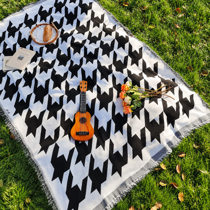 Josh & Tate - PicnicCo™ Woven Outdoor Blanket - Black and white patterned blanket with a ukulele and flowers on grass