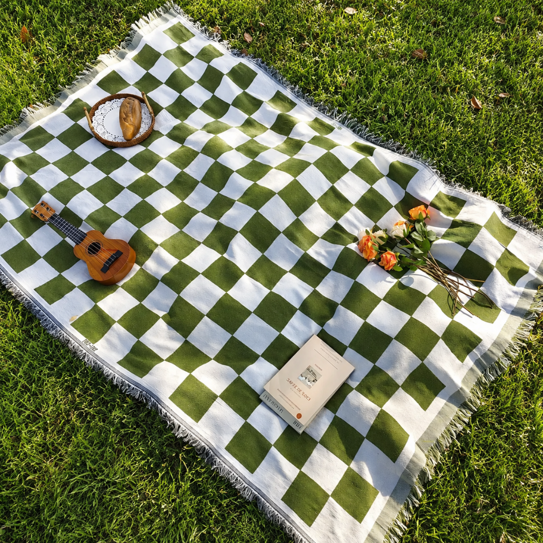 Josh & Tate - PicnicCo™ Woven Outdoor Blanket - Green and white checkered picnic blanket on grass with a ukulele, book, and flowers.