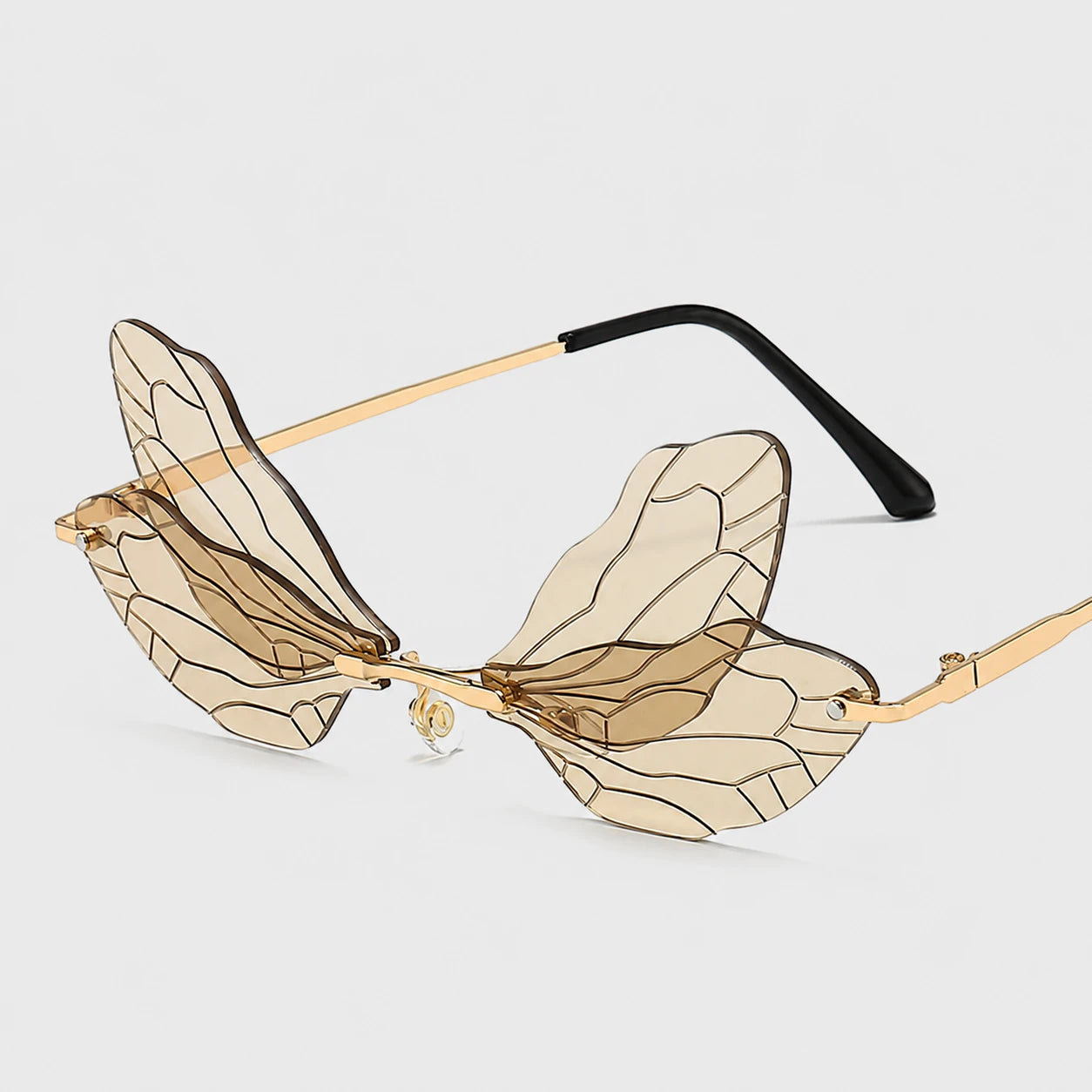 Josh & Tate - PixieFrame™ Butterfly Sunglasses - Wing-shaped sunglasses with translucent beige-tinted lenses, gold metal frames, and black temple arms, shown on a light gray background.
