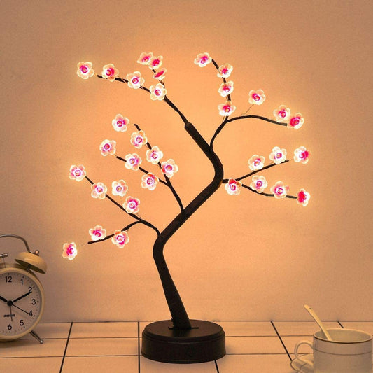 Decorative LED tree with pink flowers on a stand next to a clock and mug.