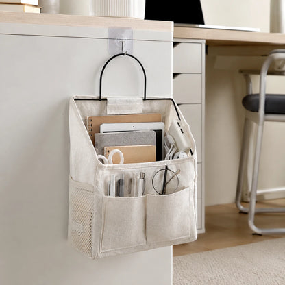 Josh & Tate - PocketPerch™ Hanging Organizer - A beige fabric desk organizer hanging from a clear hook on a white filing cabinet in a home office setting. The organizer contains various office supplies, including notebooks, pens, and glasses.