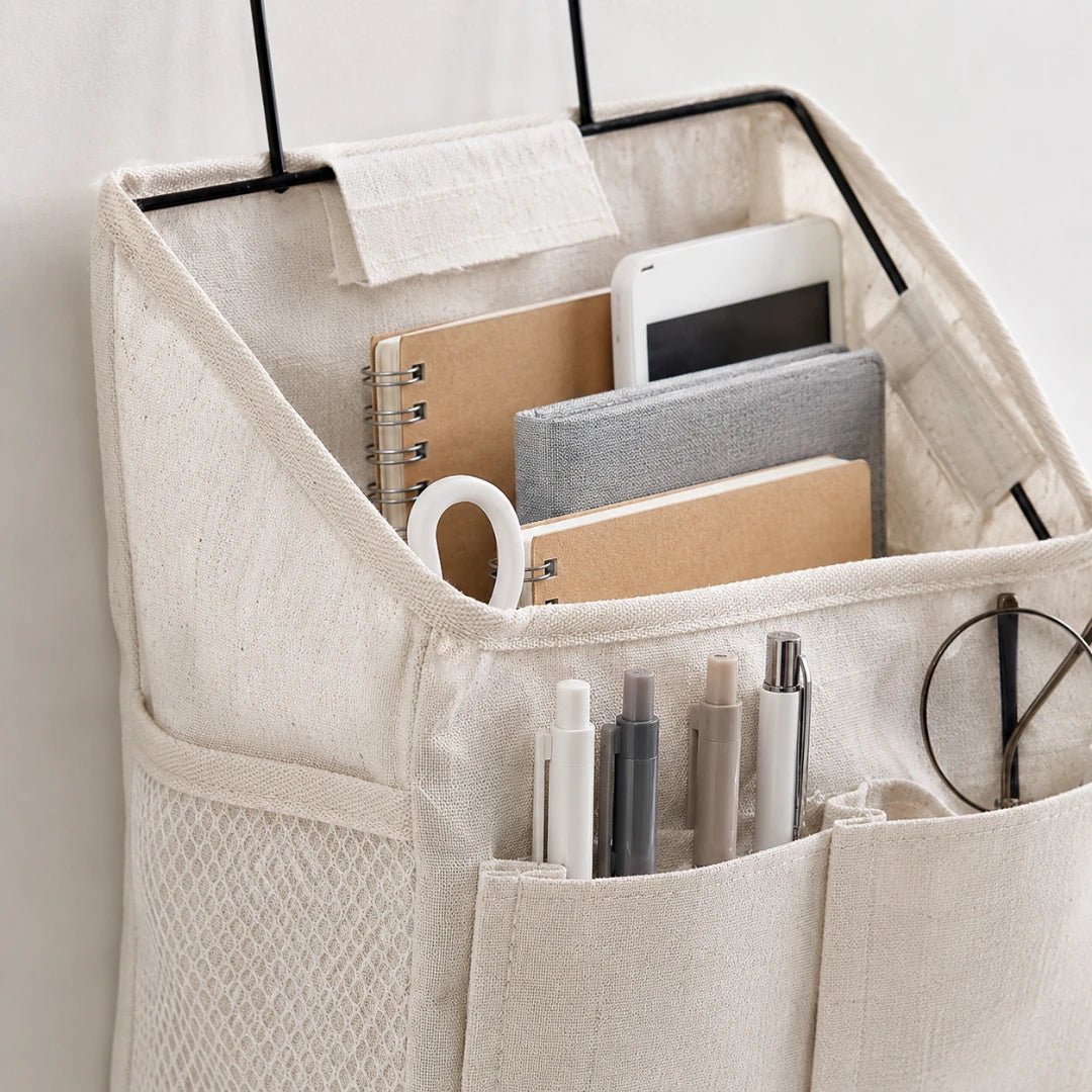 Josh & Tate - PocketPerch™ Hanging Organizer - A beige fabric desk organizer hanger with mesh pockets and a top compartment, shown holding notebooks, pens, a phone, and glasses against a light neutral background.