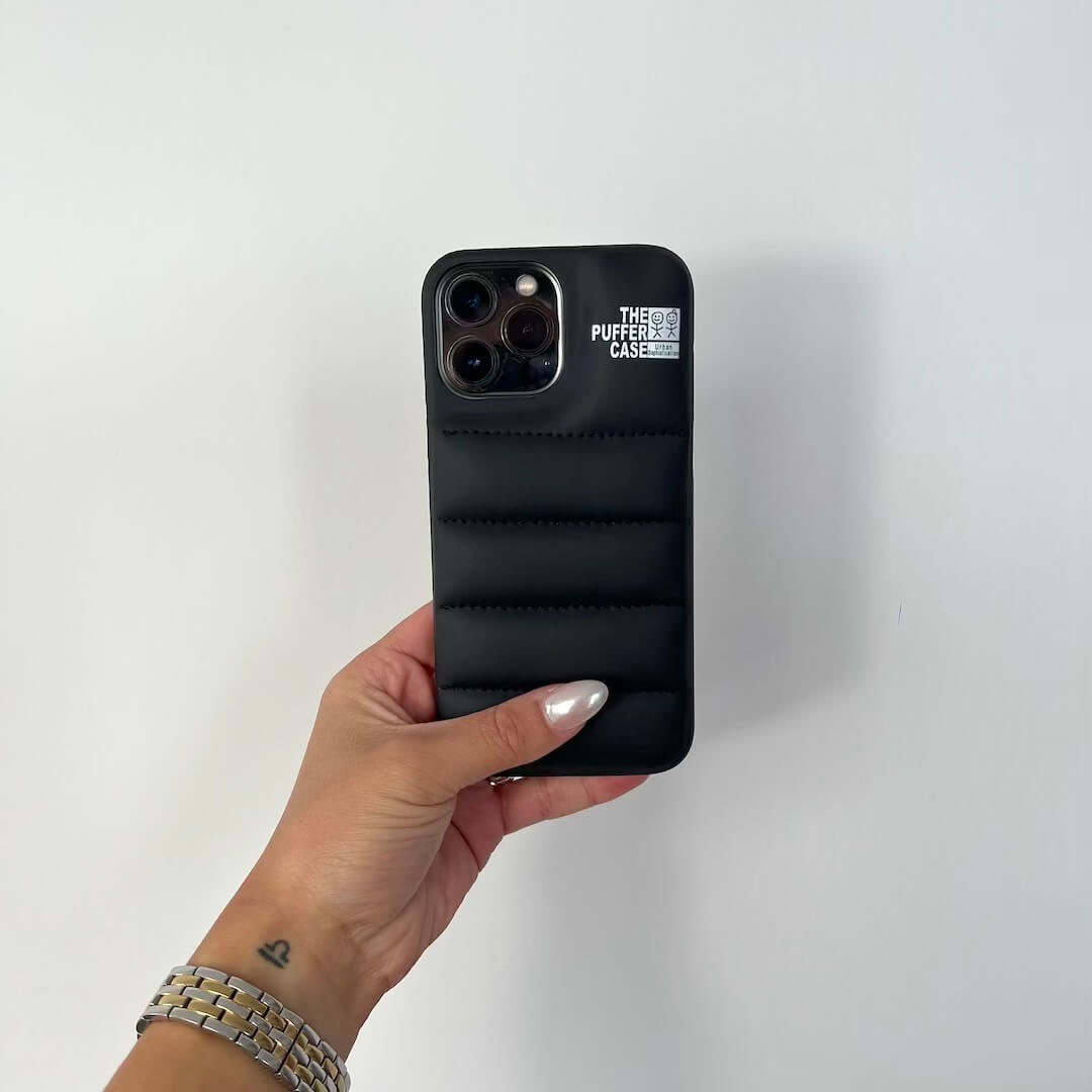 Hand holding a black phone case with 'The Puffer Case' branding on a white background