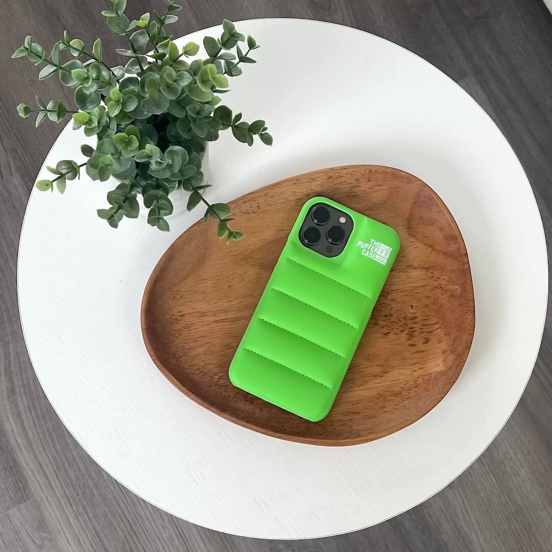Green phone case on a wooden plate with a plant on a white surface
