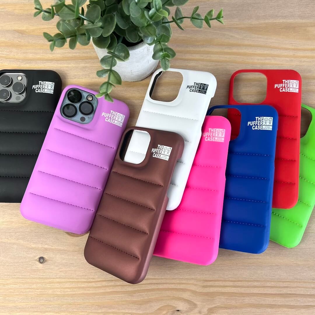 Collection of colorful phone cases on a wooden surface with a plant in the background.