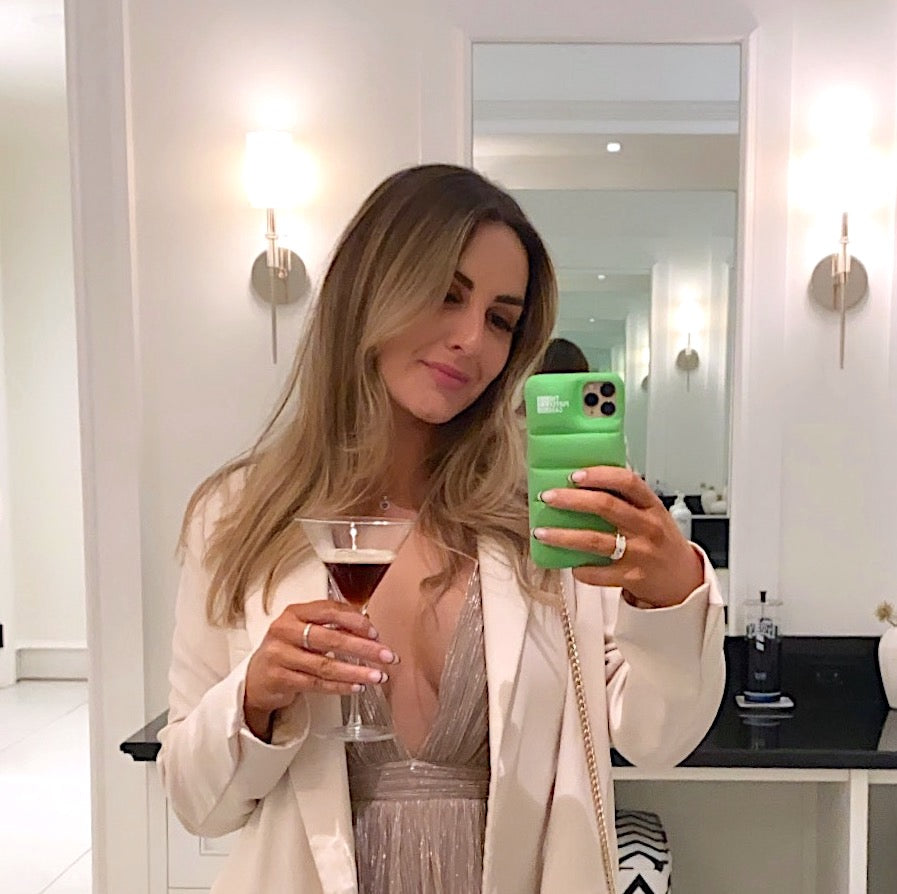 Woman taking a mirror selfie with a green phone, holding a glass of red wine.