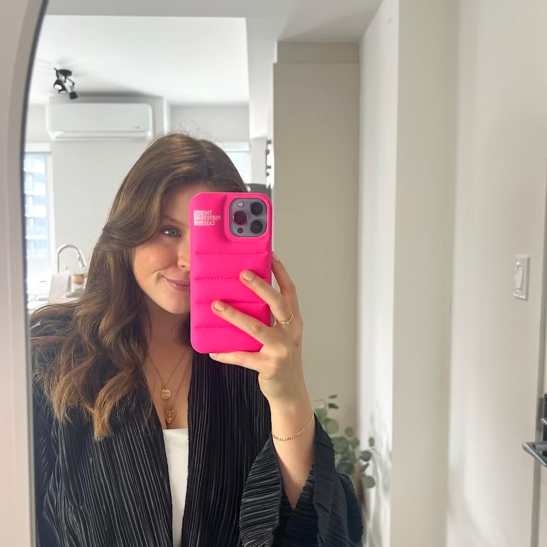Person holding a phone with a pink case in front of a mirror