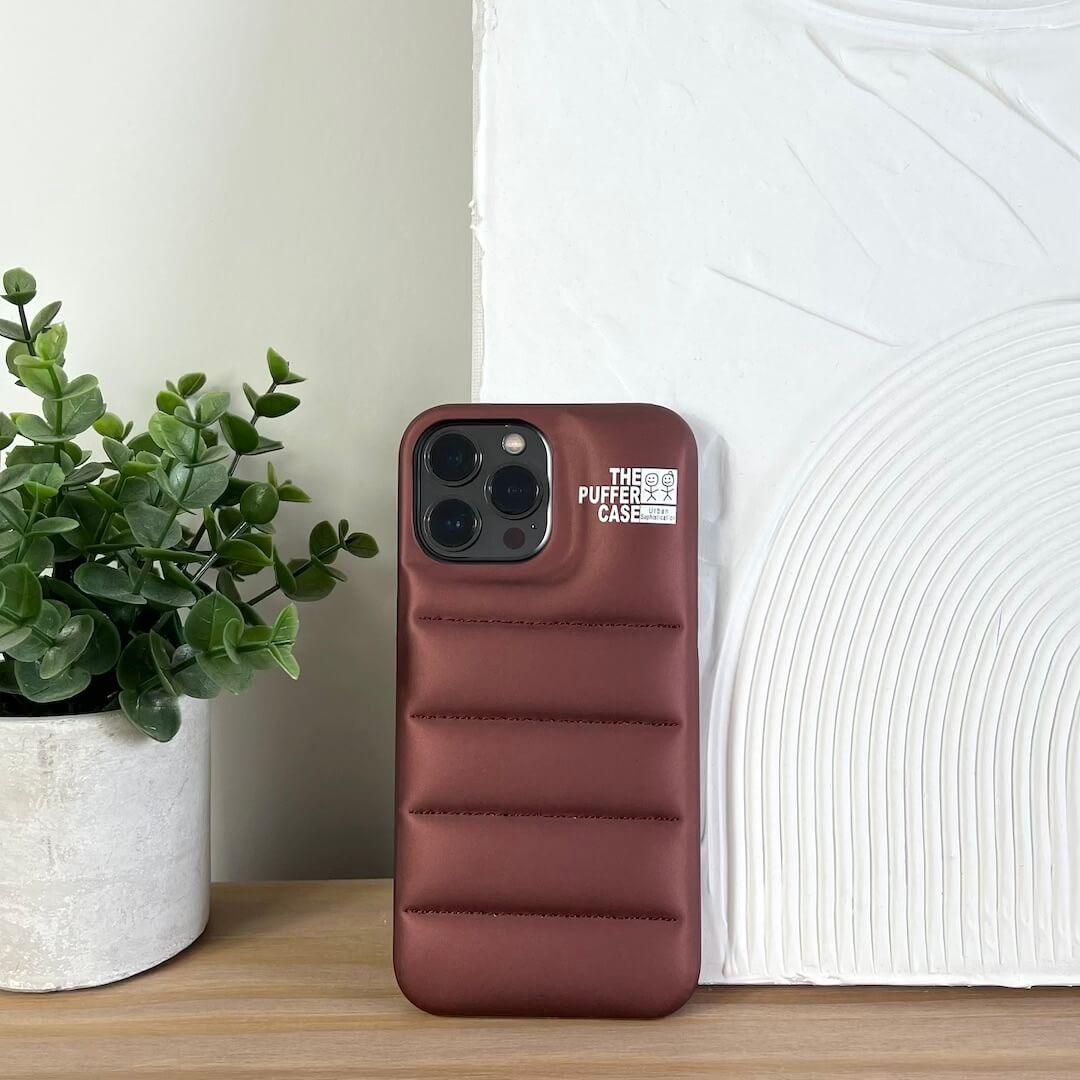 Brown phone case with brand logo on a wooden surface next to a plant