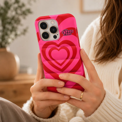 Josh & Tate - PuffHeart™ Quilted iPhone Case - Person holding a phone with a pink heart-patterned case in a cozy indoor setting