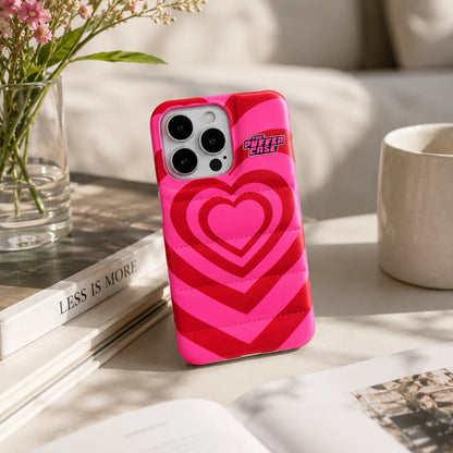 Josh & Tate - PuffHeart™ Quilted iPhone Case - Pink and red heart-patterned phone case on a table with a vase and mug in the background