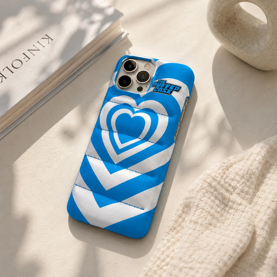 Josh & Tate - PuffHeart™ Quilted iPhone Case - Blue and white heart-patterned phone case on a light surface with a book and decorative object.