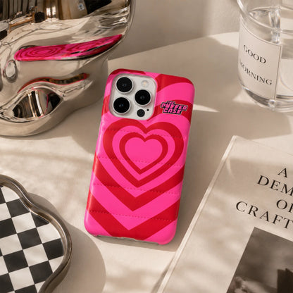 Josh & Tate - PuffHeart™ Quilted iPhone Case - Pink phone case with heart design on a surface with decorative items.