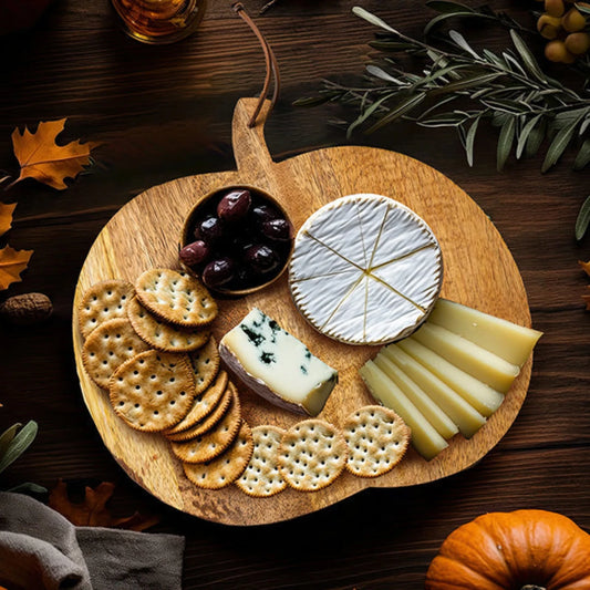 Josh & Tate - Pumpkin Wooden Cutting Board - Wooden cheese board with assorted cheeses and crackers on a wooden surface with autumn leaves.