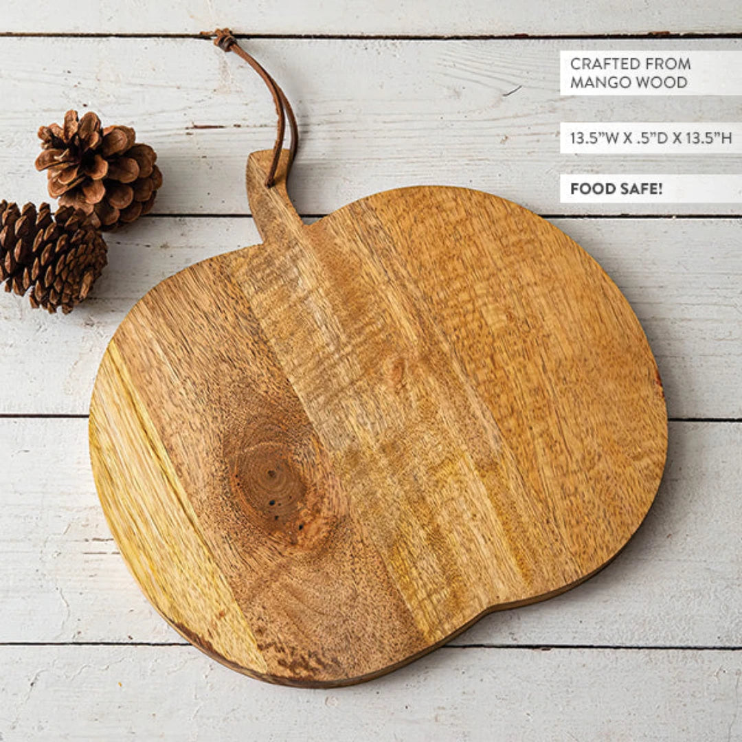 Josh & Tate - Pumpkin Wooden Cutting Board - Wooden cutting board with a handle on a light wooden surface, surrounded by pine cones.