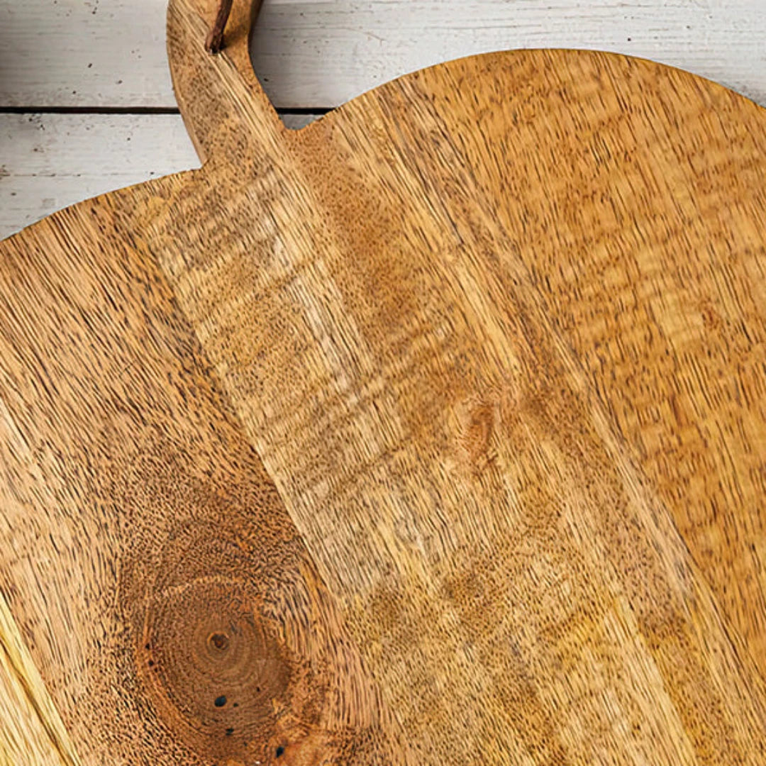 Josh & Tate - Pumpkin Wooden Cutting Board - Close-up of a wooden cutting board with a handle on a light wooden floor.