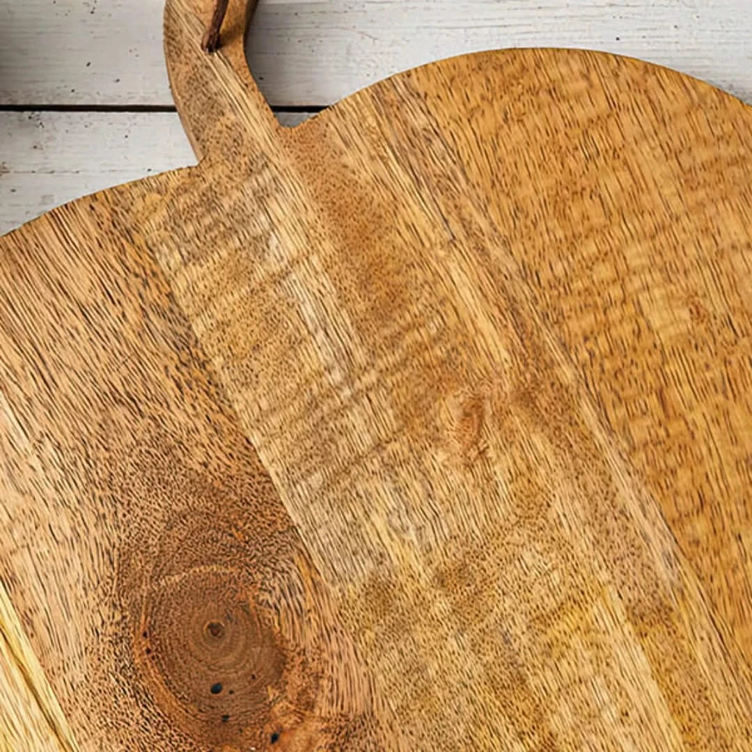 Josh & Tate - Pumpkin Wooden Cutting Board - Close-up of a wooden cutting board with a handle on a light wooden floor.
