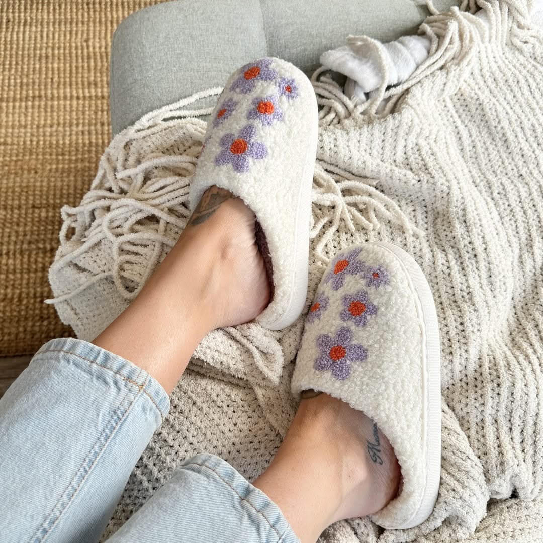 White slippers with floral patterns worn by a person on a cozy blanket.